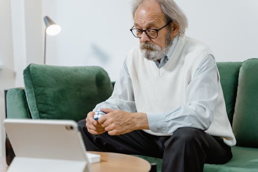 Elderly man sitting on couch, using a pulse oximeter for health monitoring.