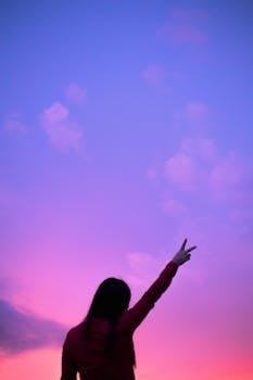 pexels-photo-8719832-8719832 Silhouette of a woman making a peace sign against a vibrant twilight sky.